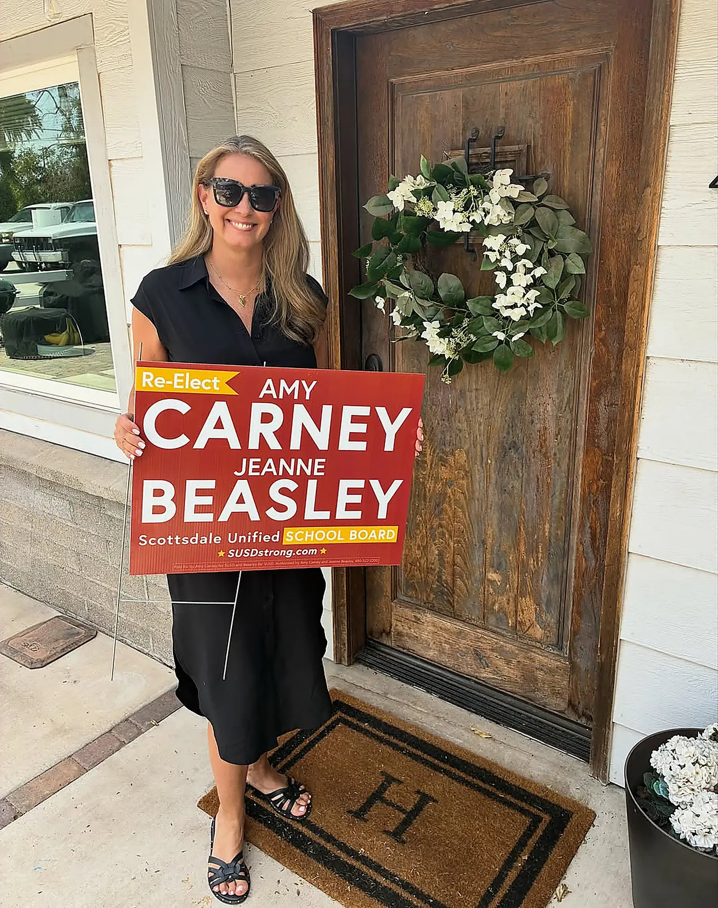 Amy Carney holding a red and yellow Carney and Beasley yard sign outside a Scottsdale home